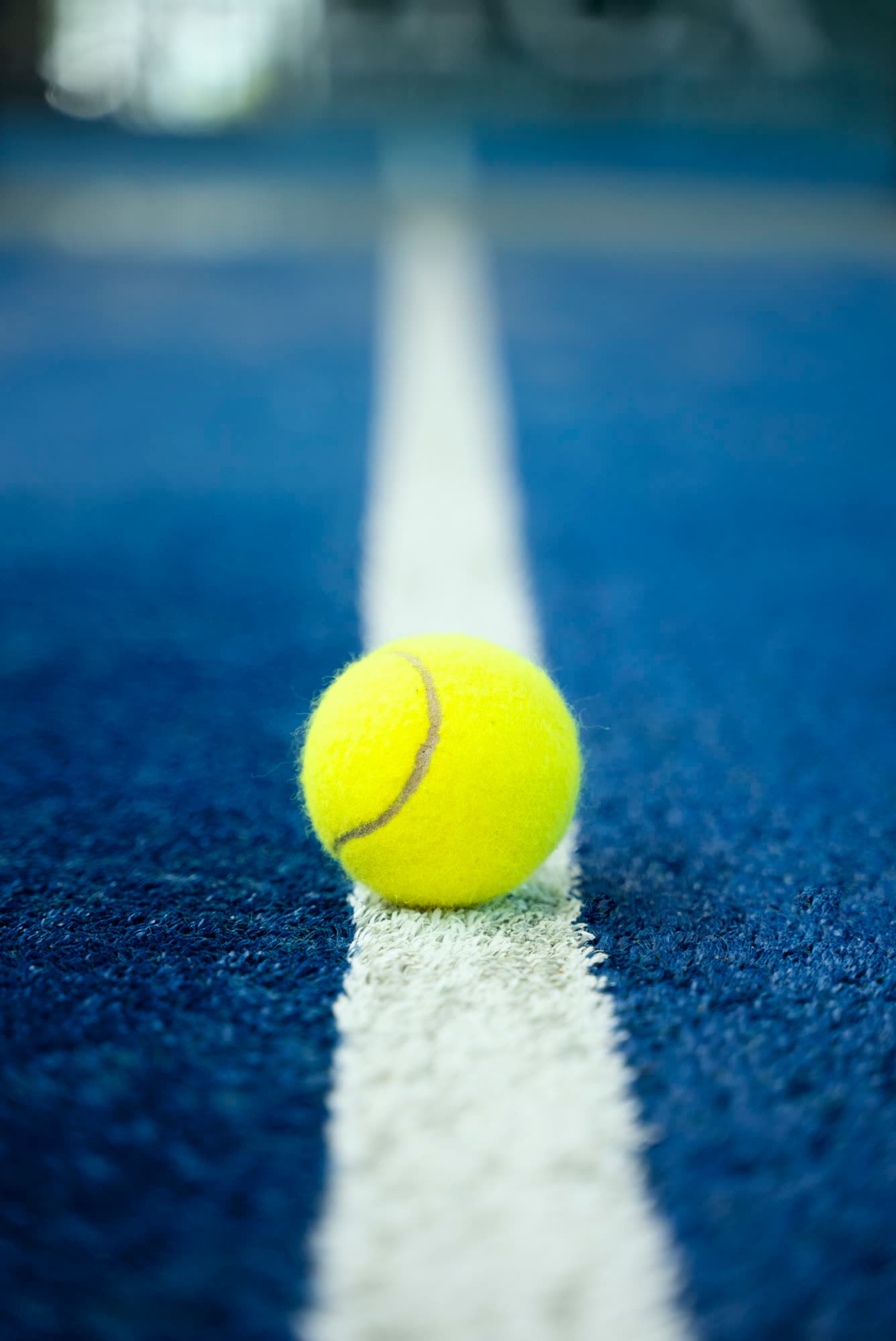 A tennis ball resting on the white line of a blue court.